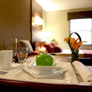 A hotel room with a room service tray featuring an apple and a vase with flowers.