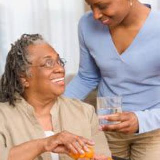 A caregiver assists an elderly woman at home with a smile.