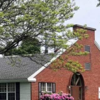 A charming brick house with a lush garden and blooming flowers under a large tree.