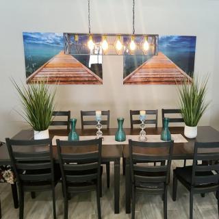 A dining room setup featuring a large table with chairs, plants as centerpieces, and scenic wall art.