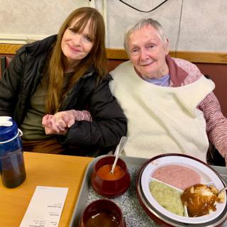 A heartwarming moment shared between a woman and an elderly person at a dining table.