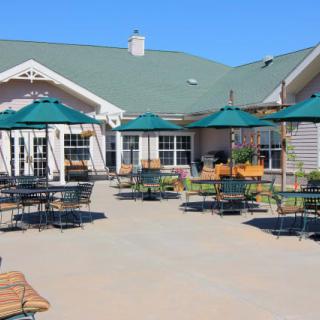 An outdoor patio area with tables and umbrellas in front of a building on a clear day.