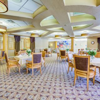 An elegant dining room with beautifully arranged tables and chairs, featuring floral decorations and ambient lighting.