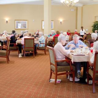 Elderly residents enjoying a meal together in a senior living dining room.