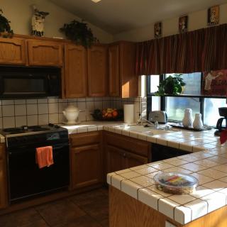A cozy kitchen with wooden cabinets, tiled countertops, and various appliances.