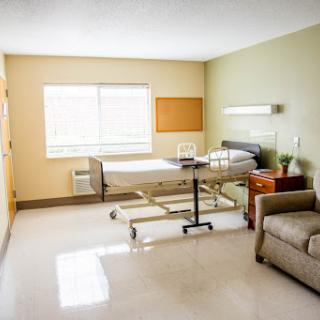 A clean and well-lit hospital patient room featuring a bed, a comfortable sofa, and natural light from the window.