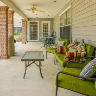 A cozy patio with green cushioned chairs, a glass table, and decorative pillows under a ceiling fan.