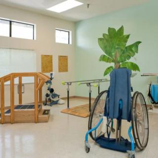 A spacious physical therapy room equipped with rehabilitation equipment, including a wheelchair.