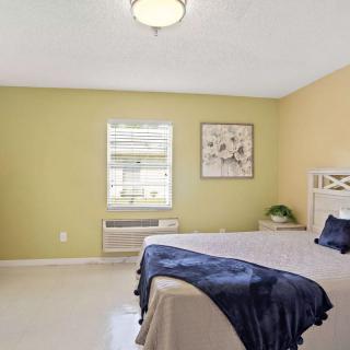 A cozy bedroom featuring a neatly made bed with blue accents, a window allowing natural light, and decorative wall art.