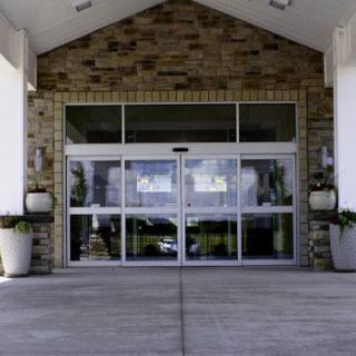 The entrance of a building featuring glass doors and a stone facade, accented by plants on either side.