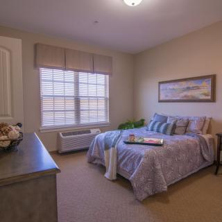 A cozy bedroom with a neatly made bed, large window, and wall artwork.