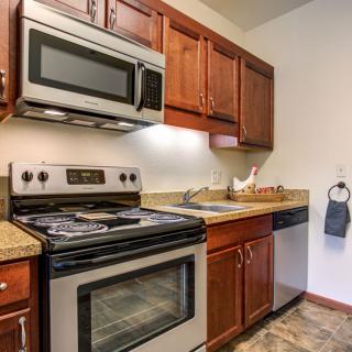 A modern kitchen with wooden cabinets, featuring an oven, microwave, sink, and dishwasher.