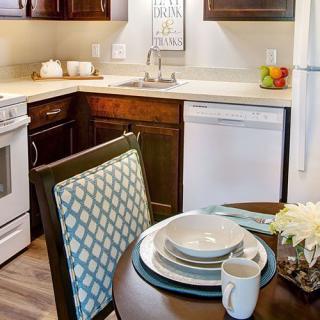 A cozy kitchen and dining area with neatly arranged dishware on the table, surrounded by modern appliances and warm decor.