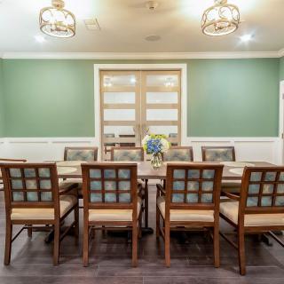 A spacious dining room with a large table surrounded by wooden chairs, featuring elegant lighting and green walls.