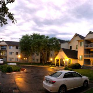 A peaceful evening view of an apartment complex with soft outdoor lighting and a cloudy sky.
