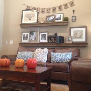 A cozy living room decorated with fall-themed elements like pumpkins and a 'welcome' banner on the shelves.