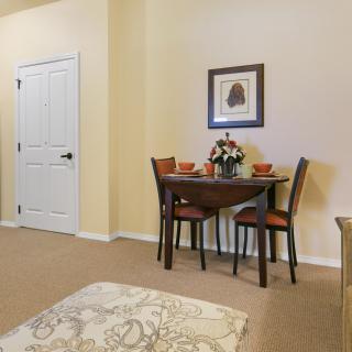 A cozy dining area with a small table set for two, featuring a floral centerpiece and artwork on the wall.