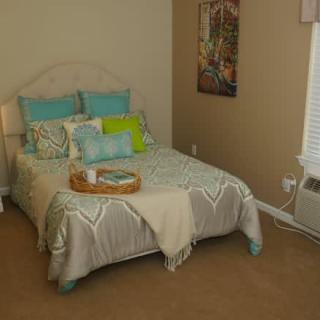 A cozy bedroom with a neatly made bed featuring blue and green pillows, a decorative tray, and a poster on the wall.