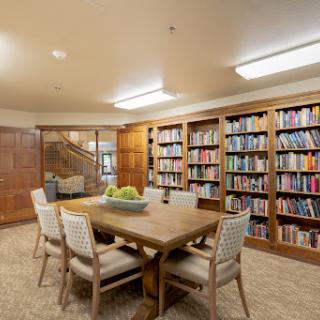 A cozy library space featuring a wooden table surrounded by chairs, with shelves filled with books.