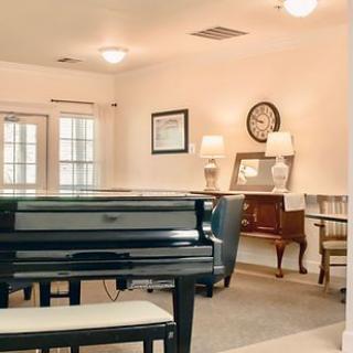 A cozy room featuring a grand piano, wall clock, lamps, and elegant furnishings.
