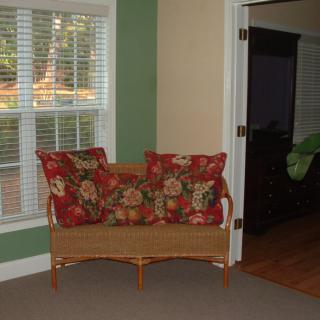 A cozy living room corner featuring a wicker loveseat with floral-patterned pillows beside a window.
