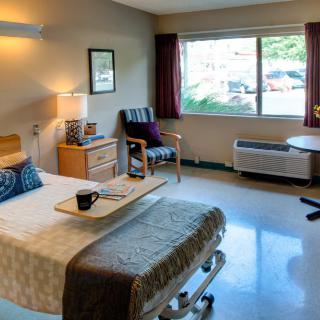 A well-lit hospital room with a bed, chair, and window.