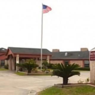 A building with an American flag flying on a pole, featuring an entrance and landscaping.
