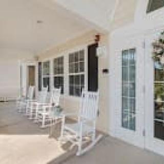 A cozy porch with white rocking chairs and large windows.