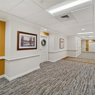 A well-lit hallway with carpeted flooring and framed artwork on the walls.