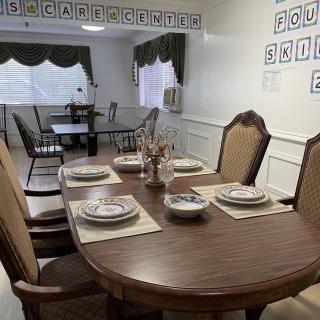 A neatly set dining room table with plates and cutlery, surrounded by chairs, in a well-lit interior space.