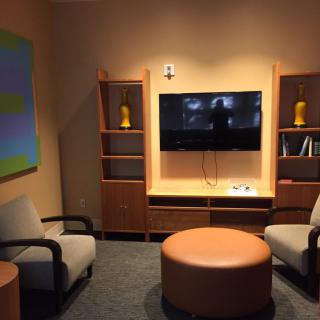 A cozy living room with modern decor, featuring a television, seating area, and shelves.