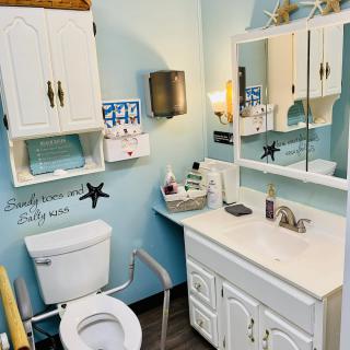 A tidy and accessible bathroom with blue walls, featuring a mirror, sink, toilet, and white cabinets.