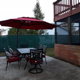 A cozy patio setup with a table, chairs, and a red umbrella in a backyard.
