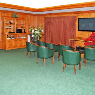 A small conference room with green chairs and wood-paneled walls, featuring a television and floral arrangement.