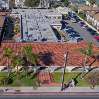 Aerial view of a building complex with a parking lot and palm trees lining the street.