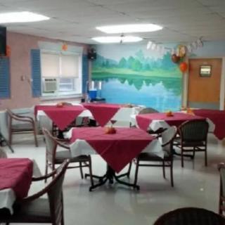 A cozy dining area with tables covered in red tablecloths, surrounded by wicker chairs and featuring a wall mural of a lakeside scene.