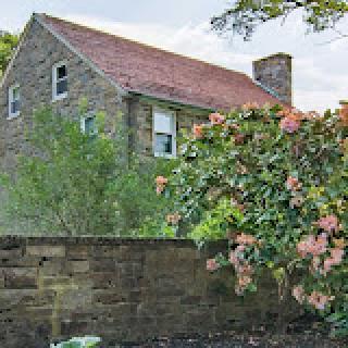 A charming stone house surrounded by lush greenery and blooming flowers.