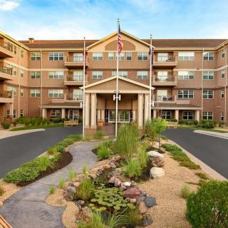 A multi-story apartment building with a landscaped entrance and flags displayed.