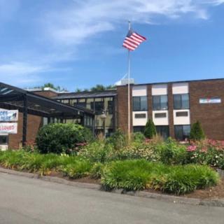 A brick school building with an American flag flying in the foreground, surrounded by a garden under a clear blue sky.
