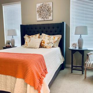 A cozy and elegantly decorated bedroom with a navy blue headboard, orange throw blanket, and matching lamps on each side.