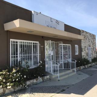 A storefront with barred windows and doors, featuring a sign above the entrance and flowers lining the sidewalk.