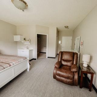 A cozy bedroom with a comfortable armchair, bed, and side lamp.