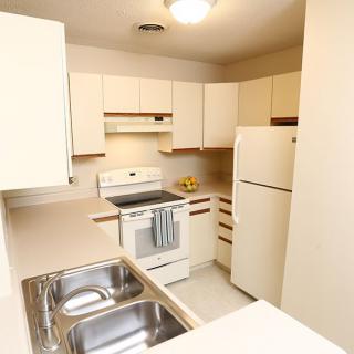 A neatly organized kitchen featuring a stove, refrigerator, and double sink surrounded by light-colored cabinetry.