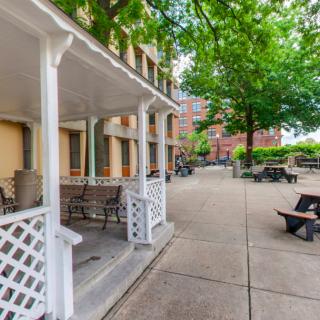 A peaceful outdoor area with benches, trees, and a building with a porch.