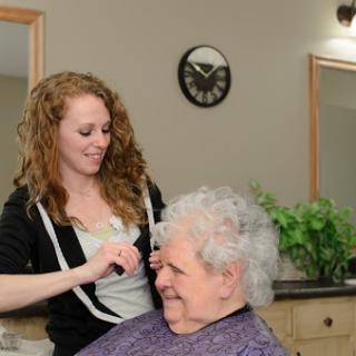 A hair stylist smiles while attending to an elderly woman in a salon setting.
