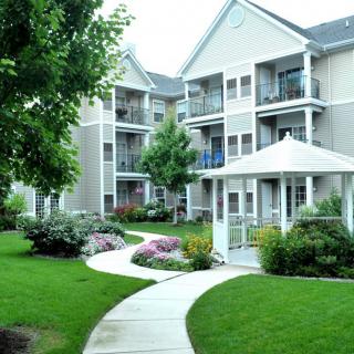A well-maintained apartment complex with lush landscaping and a winding pathway leading to a gazebo.