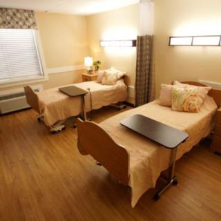 A healthcare facility room with twin beds and a wooden floor.