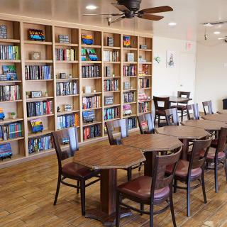 A cozy library with wooden bookshelves, a long table, and chairs for reading and activities.