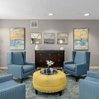 A stylish living room featuring blue armchairs and a yellow ottoman, with artwork adorning the walls.