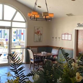 A cozy dining area with a table set for two, surrounded by plants and decorated with wall art under warm lighting.